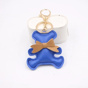 Blue PU leather bear keychain with brown bow on a minimalist white pedestal display