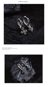 Macro detail of silver punk earrings with black zircon cross and crown heart charms