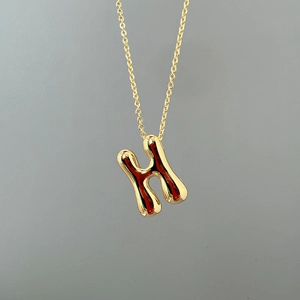 Detailed close-up of a polished gold letter H pendant necklace with a liquid metal effect