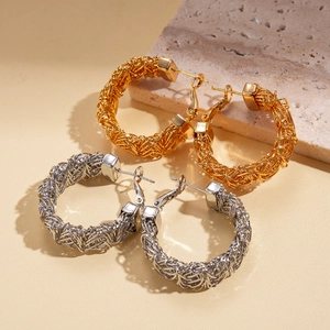 Textured gold and silver woven hoop earrings shown on a neutral stone background