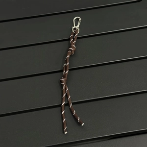 Detail of a brown woven paracord bag charm with reflective stitching and silver metal clasp