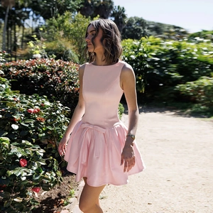 Detail of a pink sleeveless satin dress featuring a high-waisted bow and a flared skirt