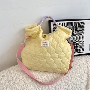 Detail van lichtgele gewatteerde canvas tas met geweven handvat en roze schouderriem