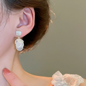Macro detail of elegant gold-tone square stud with white shell fringe hanging on ear