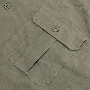 Detailed close-up of a military green linen shirt pocket with flap and button closure
