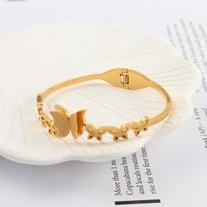 Macro detail of golden butterfly bangle with matte finish on a white shell tray
