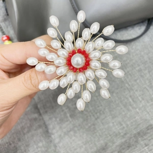 Macro shot of handmade pearl snowflake brooch with a red faceted bead center