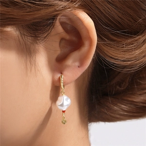 Detail of twisted gold earrings with baroque pearl and red bead on a female model