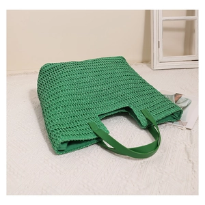 Close-up of green woven straw tote bag texture and matching faux leather handles