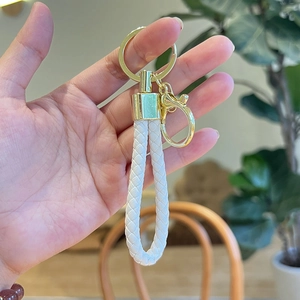 White braided leather keychain with gold metal ring held in hand with natural lighting
