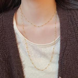 Detail of satellite chain necklace on a model wearing a brown cardigan and white top