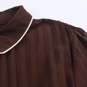 Detail of dark brown pleated midi dress featuring white contrast piping on the collar