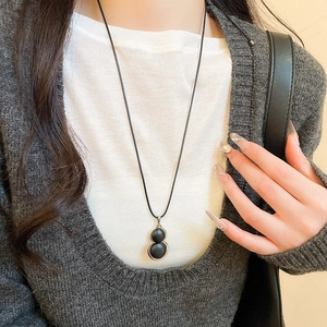 Close-up of a black gourd pendant necklace with metal trim worn on a gray sweater
