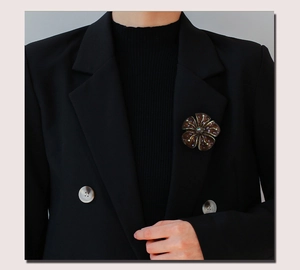 Detailed view of a vintage bronze flower brooch with enamel and pearls on a black blazer