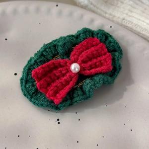 Detail of green knitted Christmas hair clip with red bow and pearl on decorative plate