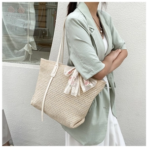 Close-up of beige straw tote bag featuring a floral lace bow decoration and woven texture