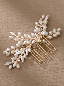 Detalle de peineta de hojas doradas con perlas blancas sobre un fondo beige