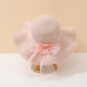 Détail d'un chapeau de paille rose avec fleur en mesh, perle et bordure ondulée