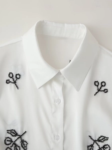 Close-up of white women's blouse featuring intricate black beaded embroidery on the collar