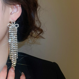 Close-up of elegant gold tassel earrings with rhinestone bow worn by a model