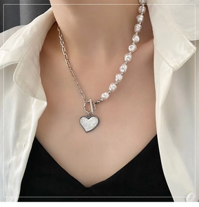 Detail view of heart pendant pearl necklace with asymmetrical silver chain and T-bar clasp