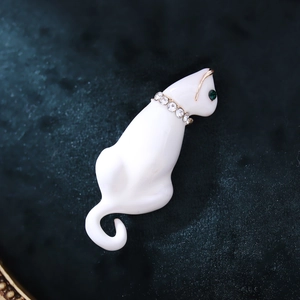 Close-up of a white enamel cat brooch with green gem eyes and a rhinestone collar