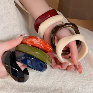 Close-up of colorful chunky acrylic bangles with wavy geometric design on a textured background