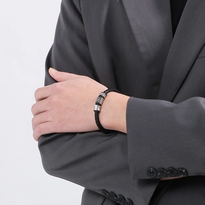 Close-up of men's black braided leather bracelet with silver clasp on model in a suit