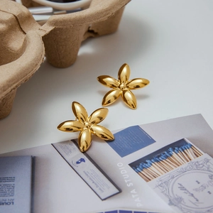 Detailed close-up of gold flower stud earrings on a minimalist magazine background