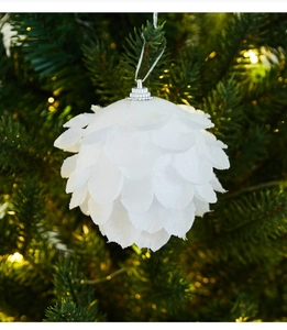 Close-up of white petal-shaped Christmas ornament with glitter on a green tree branch