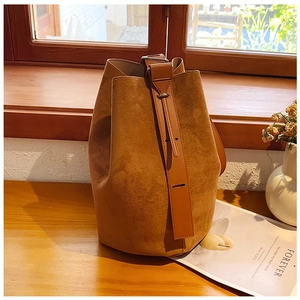 Detailed view of brown suede bucket bag texture with adjustable strap on wooden table