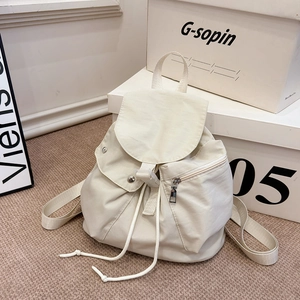 Detail view of cream nylon backpack featuring drawstring closure and front zipper pocket