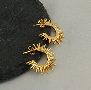 Detail view of golden C-shaped sunburst earrings on black rock surface texture