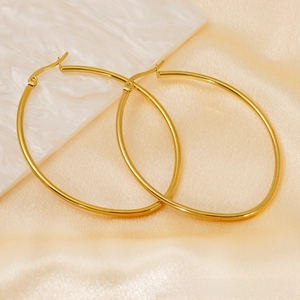 Detail of oversized gold oval hoop earrings on silk background with marble accent