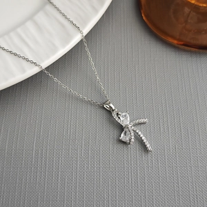 Detailed view of silver bow necklace with transparent zircon pendant on marble surface