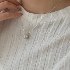 Close-up of a sterling silver hollow spherical pendant necklace worn on a striped sweater