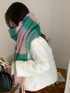 Detail of pink and green plaid scarf with thick tassels styled on a white faux fur coat