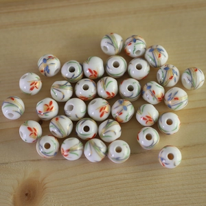 Hand-painted ceramic beads with colorful leaf patterns on light wood background