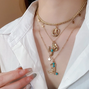 Detail of layered gold necklace with western charms like cowboy boots and horseshoe