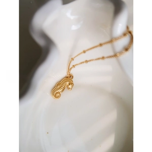 Detailed view of a gold seahorse pendant necklace with fine bead chain on white ceramic