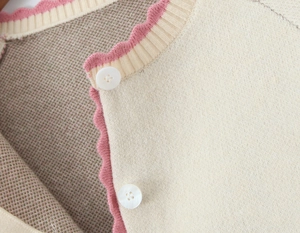Detail of knit cardigan with scalloped pink trim and glossy white buttons