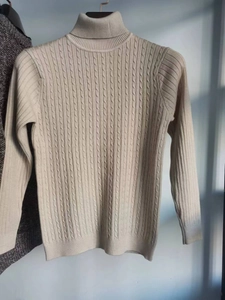 Dettaglio del maglione beige in maglia intrecciata con trama a trecce e collo alto