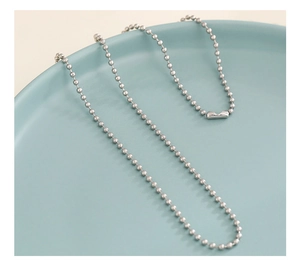 Detailed close-up of a silver beaded chain necklace displayed on a ceramic plate