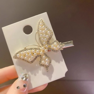 Detailed close-up of golden butterfly hair clip with white pearls and small rhinestones