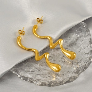 Polished gold wavy liquid metal stud earrings on a textured glass tray background