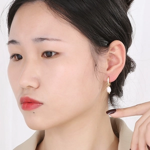 Gros plan d'un modèle portant une boucle d'oreille en perle plaquée or 18 carats et zircon