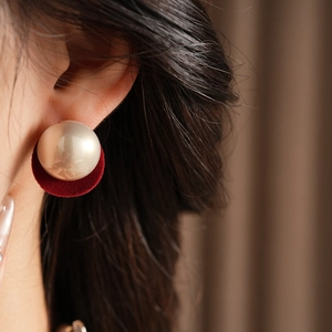 Close-up of elegant red velvet stud earrings with large beige pearls worn by a model