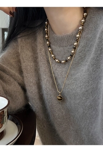 Détail d'un collier en œil de tigre plaqué or sur un mannequin en pull gris