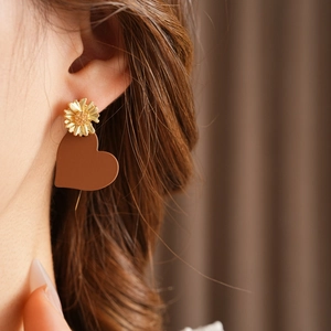 Detail shot of matte brown heart pendant and gold daisy earring on model's ear