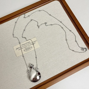 Detailed view of silver perfume bottle pendant and beaded chain on wooden display tray
